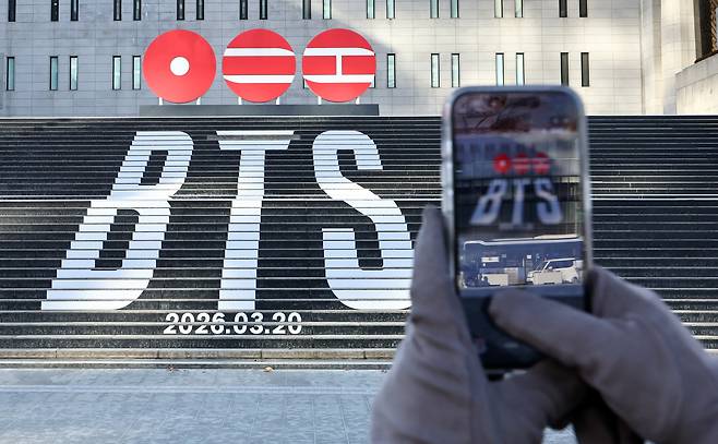 A tourist takes a photo of a promotional display for BTS's new album, ″Arirang,″ at the Sejong Center for the Performing Arts in Gwanghwamun Square in Jongno District, central Seoul on Jan. 22. [NEWS1]