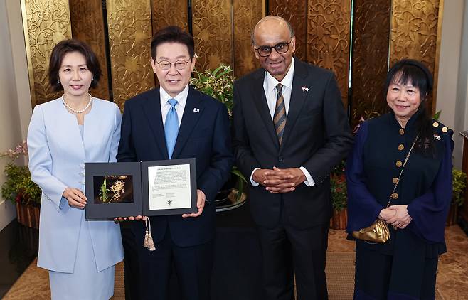 싱가포르를 국빈방문한 이재명 대통령과 김혜경 여사가 2일 싱가포르 외교부 청사에서 열린 난초 명명식에서 타르만 샨무가라트남 싱가포르 대통령, 제인 이토기 샨무가라트남 여사와 난초 증명서를 들고 기념촬영을 하고 있다.     난초 명명식은 새롭게 배양한 난초 종(種)에 귀빈의 이름을 붙이는 행사로, 난초를 국화로 삼는 싱가포르의 독특한 외교 관례다. [연합]
