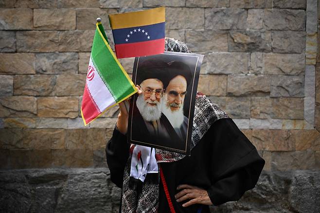 3일(현지 시각) 베네수엘라 수도 카라카스의 이란대사관 앞에 이란과 연대를 표하는 시위가 열렸다. 한 여성이 아야톨라 알리 하메네이 전 이란최고지도자의 사진과 이란 및 베네수엘라 국기를 들고 있다. / AFP=연합