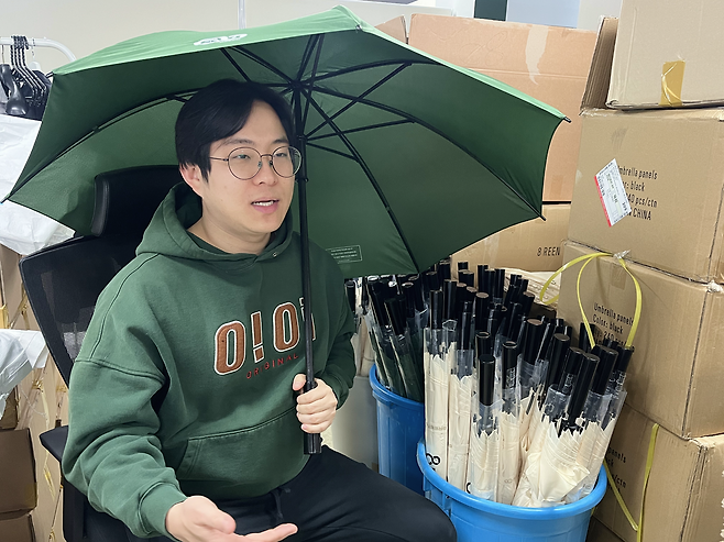 정우재 에이트린 대표가 100% 재생 플라스틱으로 제작된 우산을 쓰고 제품에 대해 설명하고 있다. 정 대표는 소비자가 우산을 분리하지 않고 버려도 재활용이 가능한 친환경 우산을 개발했다. 행복나래 제공
