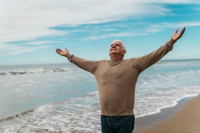 한 노인이 해변에서 양팔을 벌린 채 하늘을 바라보고 있다.<BR> 노화를 어떻게 바라보느냐가 행동과 건강 관리 방식에 영향을 줄 수 있다는 연구결과가 나와 주목을 끌고 있다.<BR> 사진=게티이미지뱅크