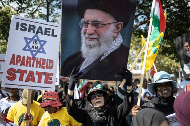 7일(현지시간) 남아프리카공화국 요하네스버그 미국 영사관 밖에서 미국, 이스라엘, 이란이 연루된 전쟁에 반대하는 시위 중 한 시위자가 고(故) 이란 최고 지도자 아야톨라 알리 하메네이의 초상이 담긴 포스터를 들고 있다.  (사진=AFP)