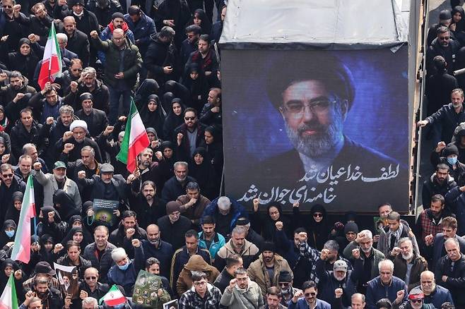 11일(현지시간) 이란 수도 테헤란에서 이란 이슬람혁명수비대(IRGC) 고위 지휘관의 장례식이 열리는 가운데 이란의 새로운 최고지도자로 선출된 모즈타바 하메네이의 사진이 걸려 있다.AFP연합뉴스