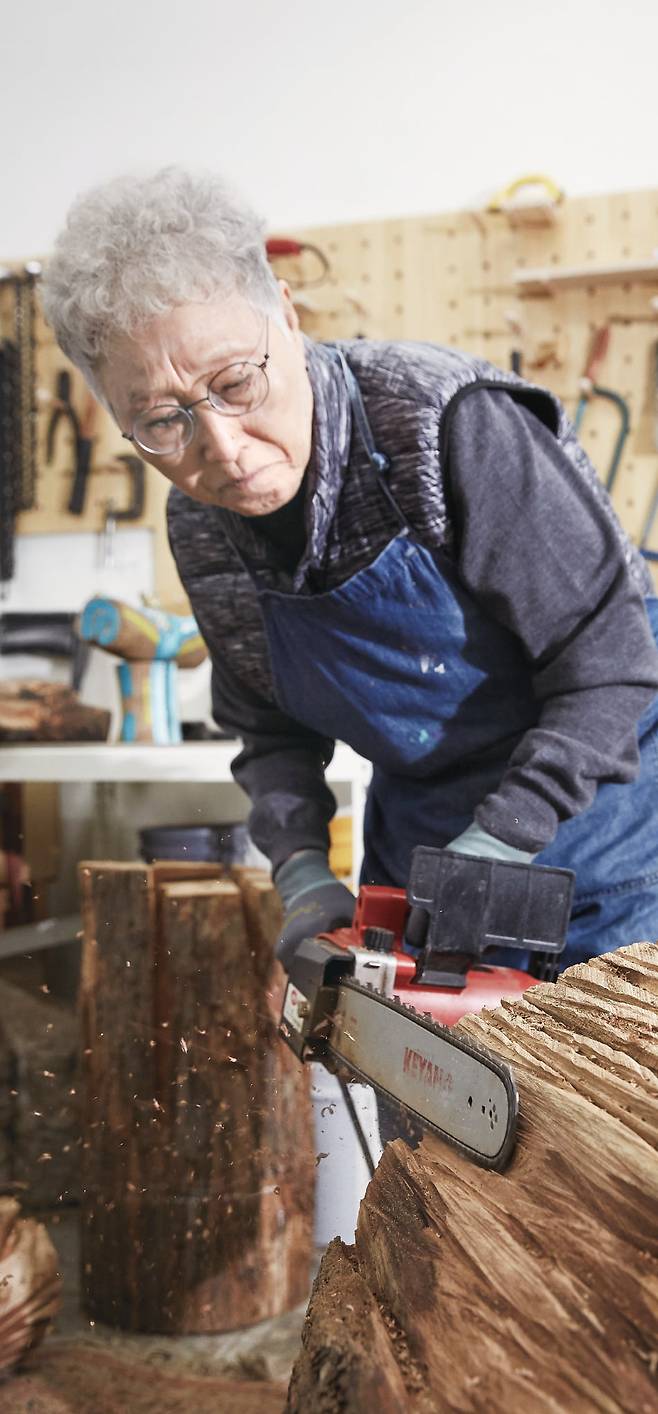 지난달 23일 경기 파주 스튜디오에서 만난 김윤신 작가. 김 작가가 “시늉만 하는 것은 의미가 없다”며 전기톱을 사용해 나무를 깎아내고 있다.  ⓒ문덕관·호암미술관 제공