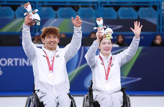 이용석(왼쪽)과 백혜진이 11일(현지시간) 이탈리아 코르티나담페초 컬링 올림픽 스타디움에서 열린 2026 밀라노·코르티나 동계패럴림픽 휠체어컬링 믹스더블 시상식에서 은메달을 목에 걸고 손을 흔들고 있다. 대한장애인체육회 제공