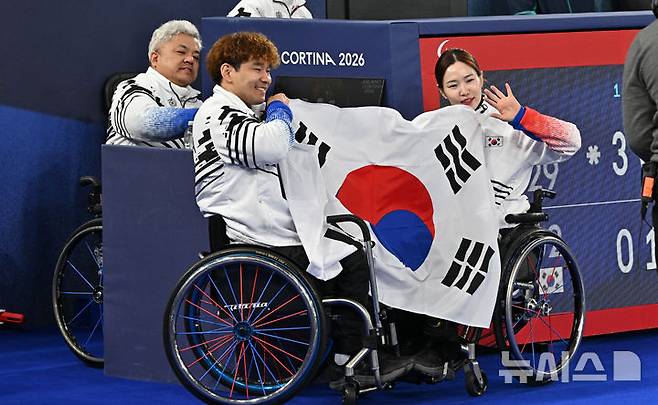 [코르티나담페초=뉴시스] 사진공동취재단 = 휠체어컬링 박길우(왼쪽부터) 감독, 이용석, 백혜진이 11일(현지 시간) 이탈리아 코르티나담페초 컬링 올림픽 스타디움에서 열린  2026 밀라노 코르티나 패럴림픽 휠체어컬링 믹스더블에서 은메달을 차지한 뒤 태극기를 들고 포즈를 취하고 있다. 2026.03.12.