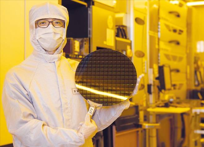 강일석 나노종합기술원 차세대플랫폼개발센터장이 12인치(300mm) 소자 반도체 웨이퍼를 들고 있다. 이 웨이퍼는 이 곳이 보유한 ASML사의 불화아르곤(ArF) 이머전 스캐너(뒤쪽 장비)를 사용해 제작했다.  /나노종합기술원 제공