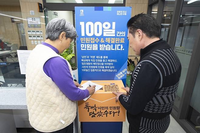 수원시가 지난해 100일간 운영한 '폭싹 담았수다! 시민의 민원함' 앞에서 시민이 민원 서류를 작성하고 있다. 사진=수원시