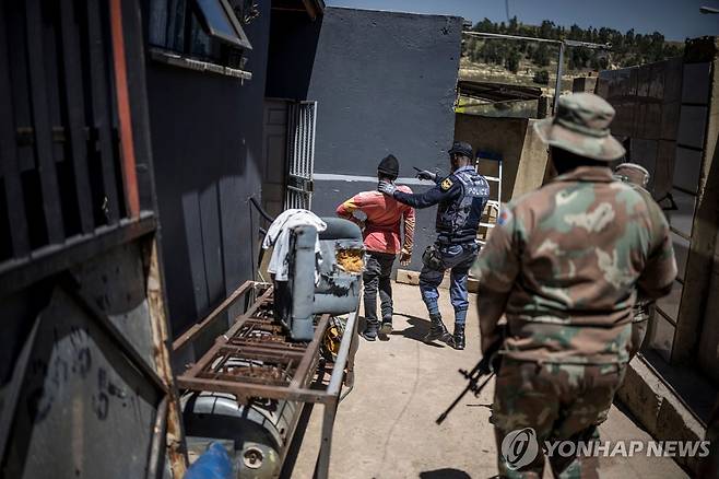 11일(현지시간) 남아프리카공화국 요하네스버그 리버리 지역에서 군인이 서 있는 가운데 경찰이 한 남성을 붙잡고 있다. [AFP=연합뉴스 자료사진. 재판매 및 DB 금지]