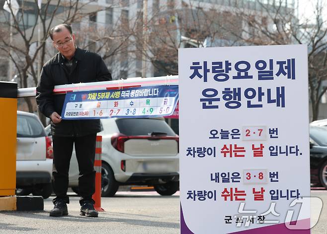 에너지 수급 위기 대응으로 공공부문 차량 5부제 전면 시행을 하루 앞둔 가운데 24일 경기 군포시 금정동 군포시청 직원주차장에서 관계자들이 차량 5부제 시행 현수막을 부착하고 있다.  2026.3.24 ⓒ 뉴스1 김영운 기자
