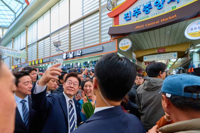 ▲ 이재명 대통령이 25일 한국항공우주산업(KAI)에서 열린 KF-21 양산 1호기 출고식에 참석한 뒤 경남 진주시 진주중앙시장을 방문해 시민과 사진을 찍고 있다. 청와대 제공