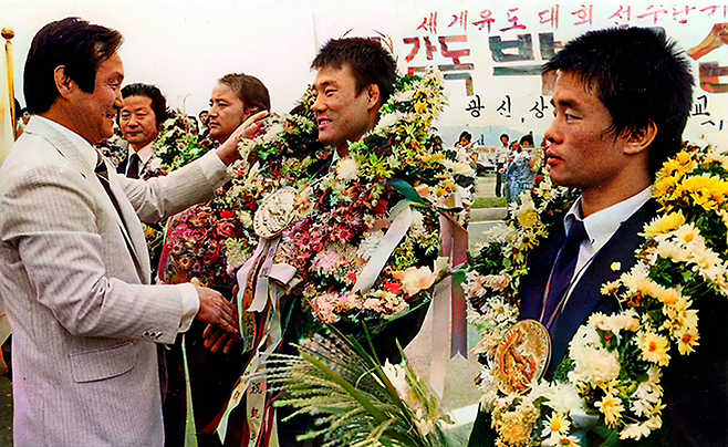 장주호 제24대 대한유도회장이 1981년 9월 제12회 국제유도연맹 세계선수권대회 금메달 획득 후 귀국한 박종학에게 화환을 걸어주며 악수하고 있다. 사진=매일경제DB(흑백)/MK스포츠(컬러화)