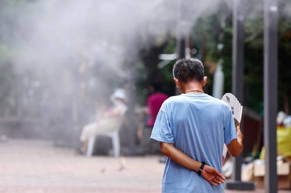 2025년 폭염 속 서울역 쪽방촌 인근 한 공원에서 주민이 쿨링포그를 맞으며 부채질을 하고년있다. [사진=연합뉴스]