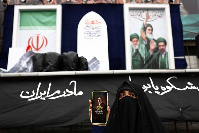 26일(현지시각) 이란 테헤란에서 한 여성이 휴대전화로 이란의 새 최고 지도자 모즈타바 하메네이의 사진을 들어보이고 있다. 테헤란/로이터 연합뉴스
