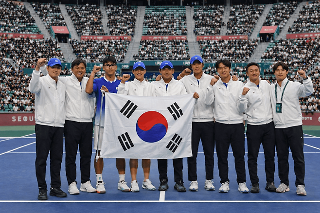 9월 열리는 한국-인도 데이비스컵 퀄리파이어 2차 라운드 경기 장소에 관한 관심이 증폭되고 있다. 서울 올림픽공원 센터코트에서 열려야 한다는 목소리가 커지고 있다. 한국 데이비스컵 대표팀이 올림픽공원 센터코트에서 환호하는 이미지를 AI로 생성.