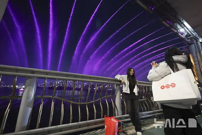 [서울=뉴시스] 김근수 기자 = 22일 저녁 서울 서초구 반포대교에서 방탄소년단(BTS) 음악에 맞춰 달빛무지개분수 뮤직 라이트쇼가 펼쳐지는 가운데 외국인들이 기념촬영을 하고 있다. 2026.03.22. ks@newsis.com