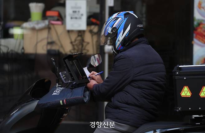 한 배달 노동자가 잠시 멈춰 서서 종이에 무언가 쓰고 있다. 한수빈 기자