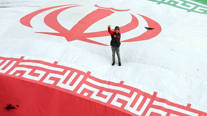 1일(현지시간) 이란 테헤란에서 미·이스라엘의 이란 공습으로 사망한 이들의 장례식이 열린 가운데 한 소년이 이란 국기 위에 서서 주먹을 불끈 쥐고 있다. AFP연합뉴스