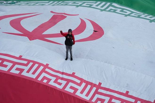 한 소년이 대형 이란 국기 위에 올라가 구호를 외치고 있다. 뉴시스