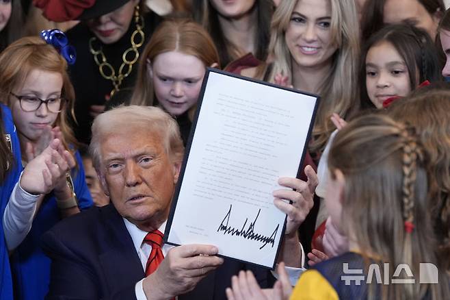 [워싱턴=AP/뉴시스] 도널드 트럼프 미국 대통령이 지난 해 취임직후인 2월 5일 백악관 이스트룸에서 여자 선수들이 지켜보는 가운데 성전환 여성 운동선수의 여성 경기 참가를 금지하는 행정명령에 서명하고 이를 들어 보이고 있다. 트럼프 대통령은 "이제부터 여성 스포츠는 여성만을 위한 것"이라고 말했고 민주당 정부의 성전환 학생 보호 협약을 모두 폐기했다. 2026.04.07.