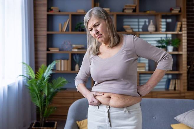 튀어나온 뱃살을 만지면서 우려하는 중년 여성. 장기 주변에 쌓이는 지방이 늘어나면 건강 위험이 커질 수 있다. 사진=게티이미지뱅크