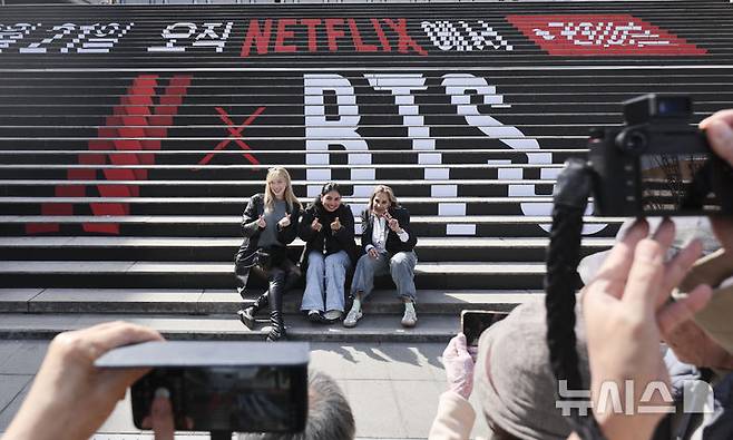 [서울=뉴시스] 황준선 기자 = BTS(방탄소년단)의 광화문광장 컴백 공연을 이틀 앞둔 19일 서울 종로구 세종문화회관 계단에 설치된 홍보물 앞에서 외국인들이 기념촬영을 하고 있다. 2026.03.19. hwang@newsis.com