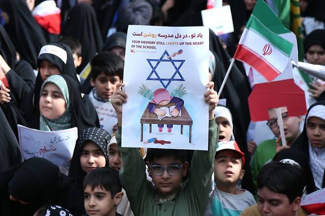 지난 7일(현지 시간) 이란 테헤란에서 열린 미사일 피격 희생 초등학생 추모 행사에 참여한 한 소년이 반이스라엘 포스터를 들어 보이고 있다. 지난 2월 28일 이란 남부 미나브의 한 여자 초등학교에 대한 공습으로 어린이 168명 포함 최소 175명이 희생됐다. AP뉴시스