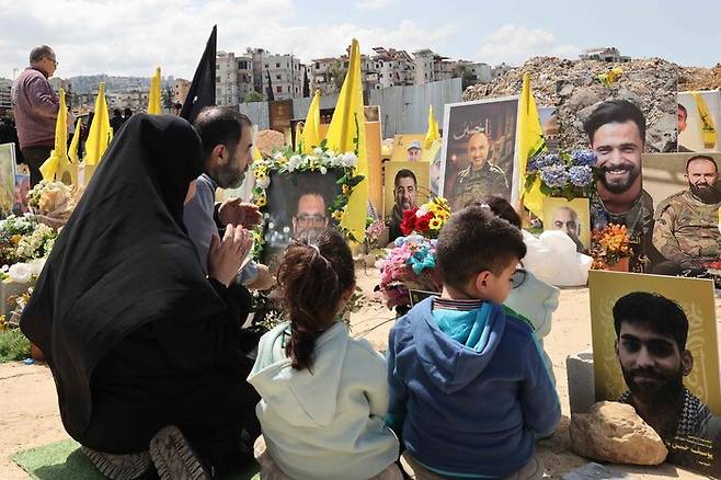 13일(현지시각) 레바논 도시 슈웨이파트의 한 묘지에서 이스라엘 공습으로 숨진 헤즈볼라 전투원과 함께 묻힌 레바논인들의 가족들이 기도하고 있다. AFP 연합뉴스