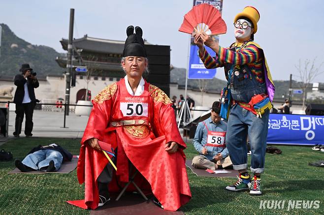 14일 서울 광화문광장에서 열린 ‘2026 광화문 멍때리기 대회’에서 관계자가 세종대왕 복장을 한 참가자에게 부채질을 하고 있다.