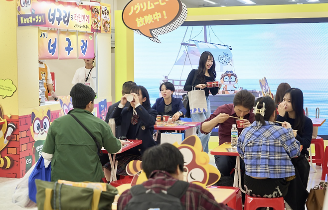 지난 16일 일본 도쿄에서 개막한 ‘2026 코리아 엑스포 도쿄’에서 농심이 ‘너구리’를 주제로 연 부스에서 방문객들이 라면을 시식하고 있다.  농심 제공