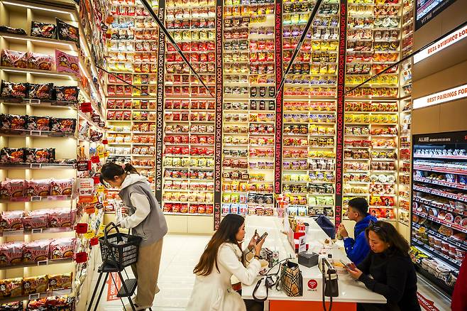 Visitors eat instant noodles beside a wall of ramyeon products at Emart24’s K-Food Lab in Myeong-dong on April 3. (Newsis)