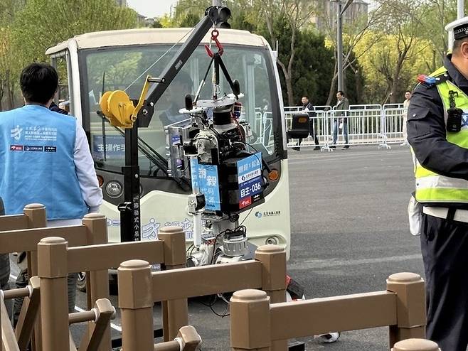 19일 ‘2회 베이징 이좡 인간형 로봇 하프마라톤 대회’에 참가한 로봇이 분리대에 부딪혀 넘어져 거치대에 걸려 있다. 베이징/이정연 특파원