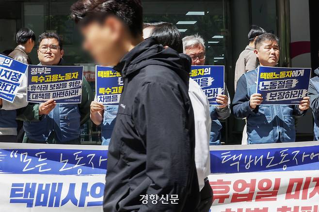 전국택배노조 소속 조합원들이 24일 서울 중구 서울지방고용노동청 앞에서 ‘택배사의 노동절 휴업일 미지정 규탄 및 특수고용노동자 차별 철폐 기자회견’을 연 가운데 인근 직장인들이 앞을 지나가고 있다.