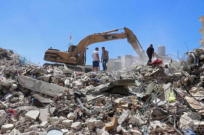 23일(현지시간) 레바논 남부 티르의 한 주거 지역에서 주민 모하마드 알리 히자지(왼쪽)가 무너진 건물 잔해를 치우는 굴착기 옆에 서 있다. 그는 이스라엘의 공습으로 목숨을 잃은 가족들의 유품을 찾기 위해 잔해 더미를 뒤지고 있었다. 2026.04.23. ⓒ AFP=뉴스1