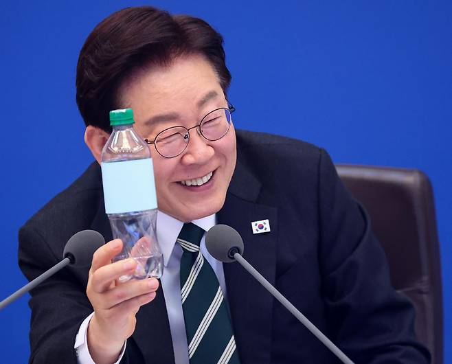 이재명 대통령이 28일 청와대에서 열린 제18회 국무회의 겸 제6차 비상경제점검회의에서 김성환 기후에너지환경부 장관 발언 때 100% 재활용 플라스틱 용기를 들고 있다. 뉴스1