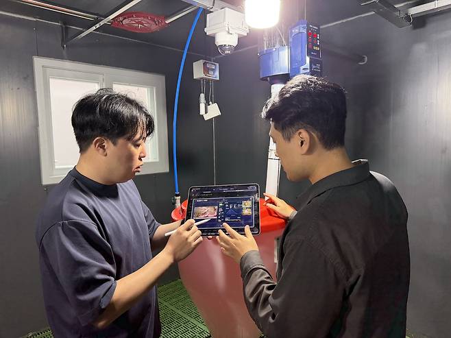 ETRI 연구진이 ‘제주형 양돈 AX 스마트팜’ 현장에서 스마트 기기를 이용해 돈사 내부 환경 제어 시스템을 점검하고 있다.[ETRI 제공]