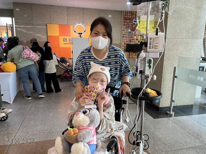 희귀질환 신경섬유종 환우 김하주양이 휠체어에 앉아 어머니 김희진씨와 찍은 사진을 들고 웃고 있다. 이지 수습기자