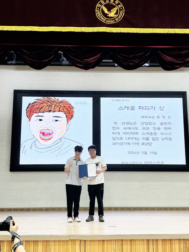 ▲ 의성고 학생회장 황성준 학생(왼쪽)이 지난 15일 스승의 날 행사를 맞아 윤영준 체육교사에게 학생들이 직접 제작한 이색 표창장을 전달한 뒤 기념촬영을 하고 있다. 이날 학생들은 손그림 캐리커처와 재치 있는 문구가 담긴 감사 영상을 준비해 교직원들의 웃음과 박수를 이끌어냈다. 의성고 제공