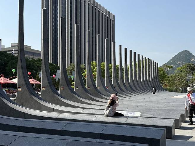 지난 16일 서울 광화문광장의 '감사의 정원' 석조 조형물 위에 한 시민이 걸터앉아 사진을 찍고 있다. 사진=이창훈 기자