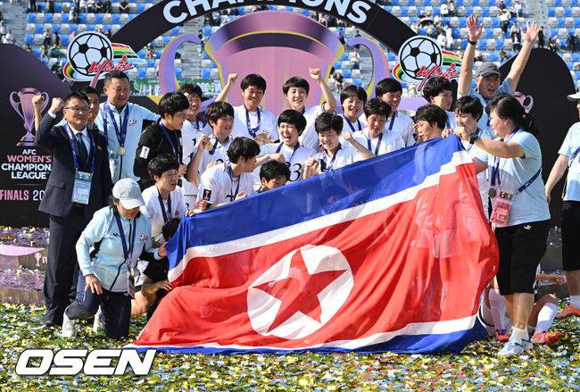 [OSEN=수원, 이대선 기자] 우승컵도, 100만 달러(약 15억 원) 우승 상금도 북한 내고향여자축구단 차지가 됐다. 논란 속 한국에서 열린 결승전에서 내고향은 일본 도쿄 베르디 벨레자를 꺾고 아시아 정상에 올랐다. 경기장 분위기 역시 마지막까지 씁쓸함을 남겼다.내고향은 23일 오후 수원종합운동장에서 열린 2025-2026 아시아축구연맹(AFC) 여자 챔피언스리그(AWCL) 결승전에서 도쿄 베르디를 1-0으로 꺾고 우승을 차지했다. 이날 공식 관중은 2670명이었다.경기 종료 후 내고향여자축구단 선수단이 인공기를 펼치고 기념촬영을 하고 있다. 2026.05.23 /sunday@osen.co.kr