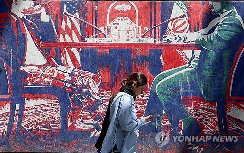 26일(현지시간) 이란 테헤란의 옛 미국 대사관 인근에서 한 이란 소녀가 미국과 이란의 협상 테이블을 묘사한 반미(反美) 벽화 곁을 지나가고 있다. [EPA 연합뉴스. 재판매 및 DB 금지]