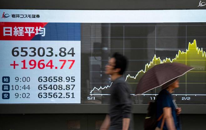 25일(현지 시간) 일본 도쿄의 한 거리에서 보행자들이 도쿄 증권거래소의 닛케이 평균주가가 표시된 전광판 앞을 지나가고 있다. AFP연합뉴스