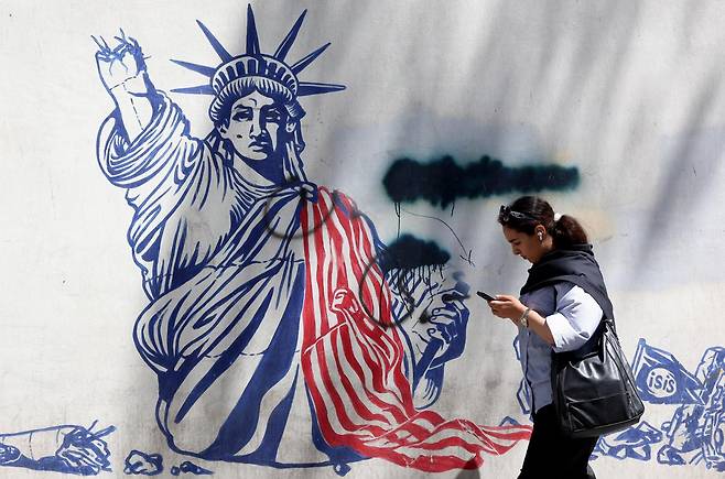 한 이란 여성이 26일 이란 테헤란 미국 대사관이 있었던 건물 앞을 지나가고 있다. 건물 외벽에는 미국을 규탄하는 내용의 벽화가 그려져 있다. 테헤란=EPA 연합뉴스
