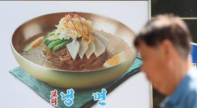 서울 마포구의 한 식당에 붙은 냉면 메뉴 사진 앞으로 시민이 지나고 있다. /사진=연합뉴스
