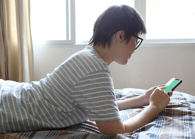 한 청소년이 침대에 엎드려 스마트폰을 보고 있다. 영국 조사에서 10대 남학생들이 AI 챗봇을 친구나 연애 상대로 받아들이는 흐름이 확인됐다. 기사 내용과 직접 관련 없음. 123rf