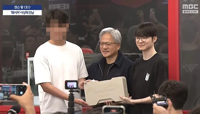 젠슨 황 엔비디아 CEO(가운데)가 프로게이머 페이커(오른쪽)와 함께 엔비디아의 최신 그래픽 카드 ‘지포스 RTX 5090’에 직접 사인한 뒤 추첨을 통해 현장에 있던 한 시민에게 선물로 증정했다. [MBC]