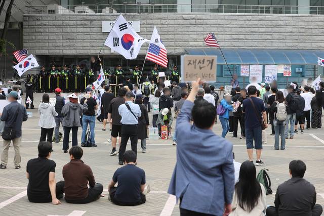 6·3 지방선거 투표용지 부족 사태를 규탄하며 재선거를 요구하는 ‘잠실 개표소 봉쇄 시위’가 계속되고 있는 8일 서울 송파구 올림픽공원 핸드볼경기장 출입구 앞에서 참가자들이 구호를 외치고 있다. [연합뉴스]