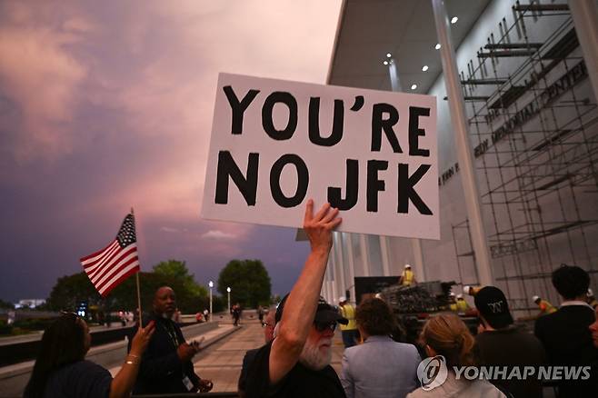 케네디센터 앞에 모인 시민 (워싱턴 AFP=연합뉴스) 13일(현지시간) 도널드 트럼프 대통령의 이름을 철거한 작업이 진행된 케네디센터 앞에서 한 시민이 '너는 JFK가 아니야'라는 팻말을 들고 있다. 2026.6.13 photo@yna.co.kr