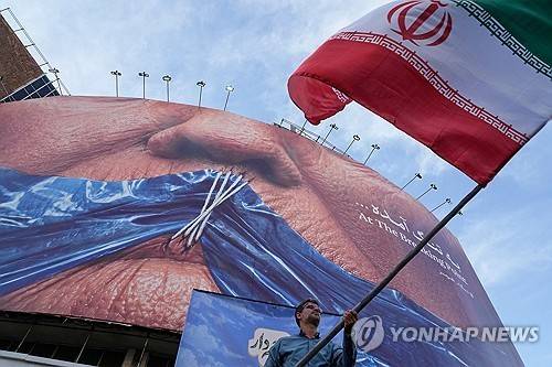 이란 수도 테헤란의 한 광장에서 호르무즈 해협과 입이 꿰매진 도널드 트럼프 미국 대통령의 모습이 그려진 광고판 아래에서 한 남성이 이란 국기를 흔들고 있다. [AP 연합뉴스 자료사진. 재판매 및 DB 금지]