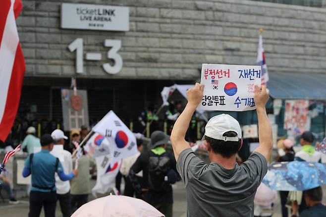 6·3 지방선거 투표용지 부족 사태로 인한 ‘개표소 봉쇄 시위’가 계속되고 있는 지난 18일 서울 송파구 올림픽공원 핸드볼경기장 출입문 앞에서 참가자들이 구호를 외치고 있다. [연합뉴스]